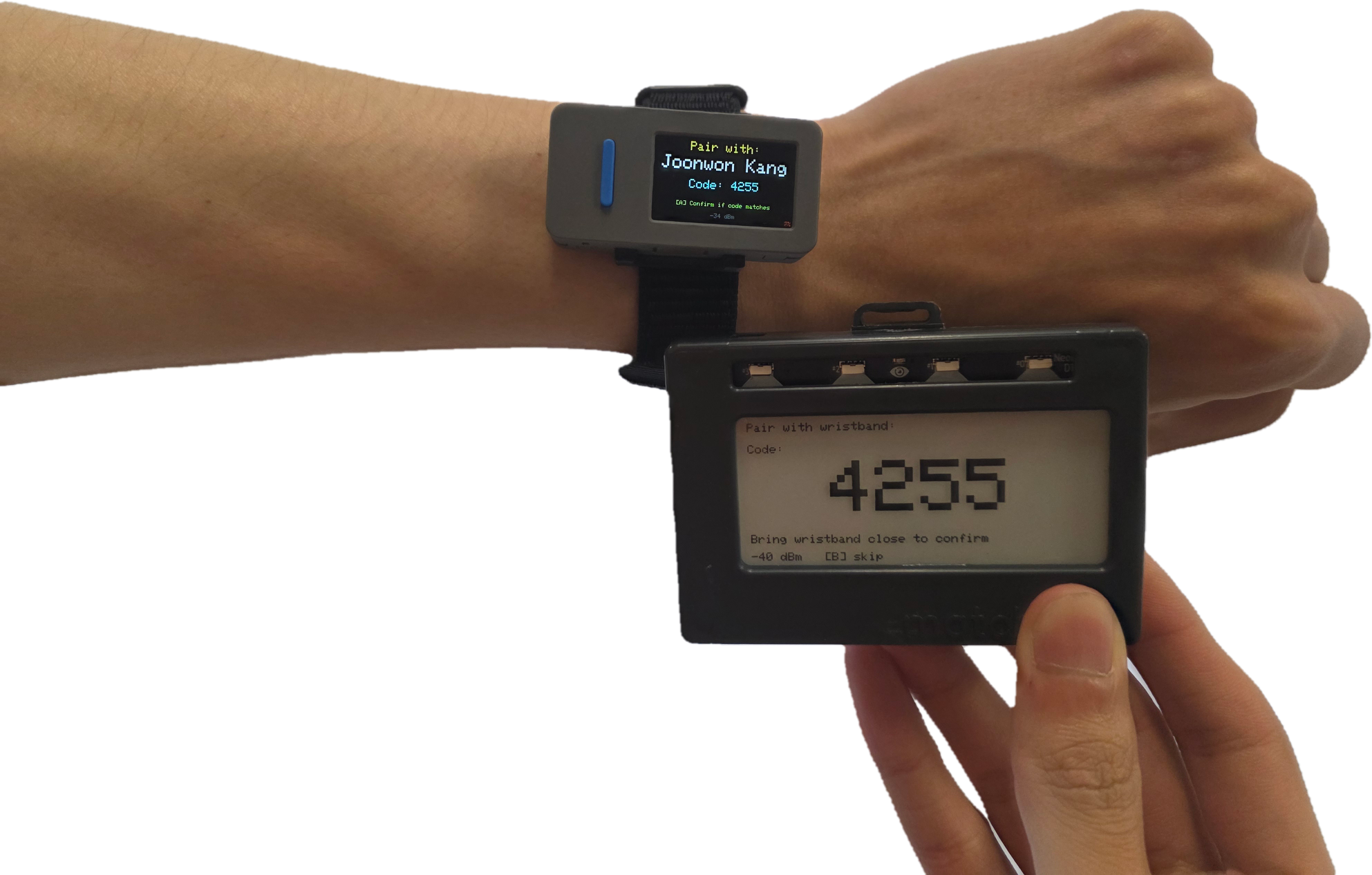 A wristband showing a four-digit pairing code and the name it will pair with, held next to a badge displaying the same code